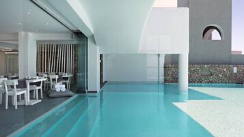 A modern indoor pool area with a dining setup and a stone wall.