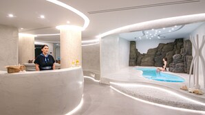 Un área de spa moderna con piscina, una recepción y una persona sentada junto a la piscina.
