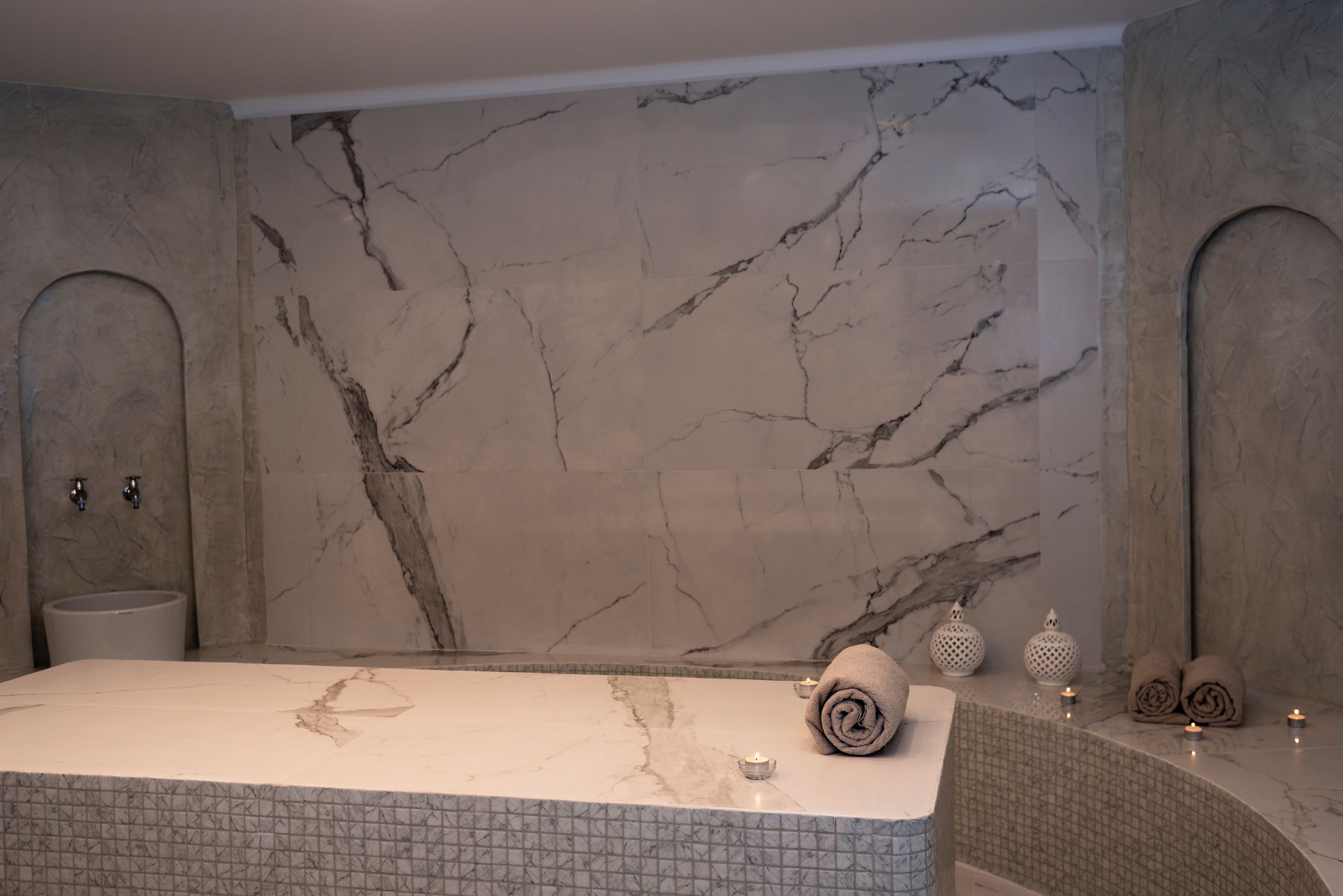 A bathroom with a marble bathtub, a sink, and a wall with a marble pattern.
