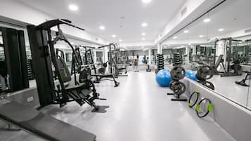 Un gimnasio moderno con diversos equipos de ejercicio, un espejo grande y una banca.