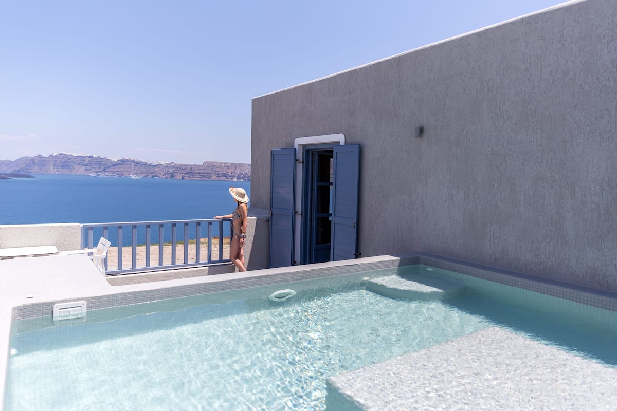A swimming pool with a view of the sea, a beach chair, and a door to a room.