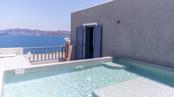 A swimming pool with a view of the sea, a beach chair, and a door to a room.