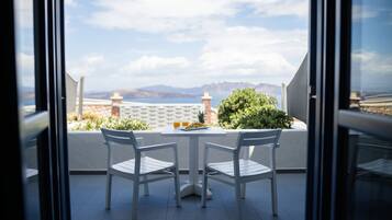 A balcony with two white chairs, a small table, and a view of the sea and mountains.