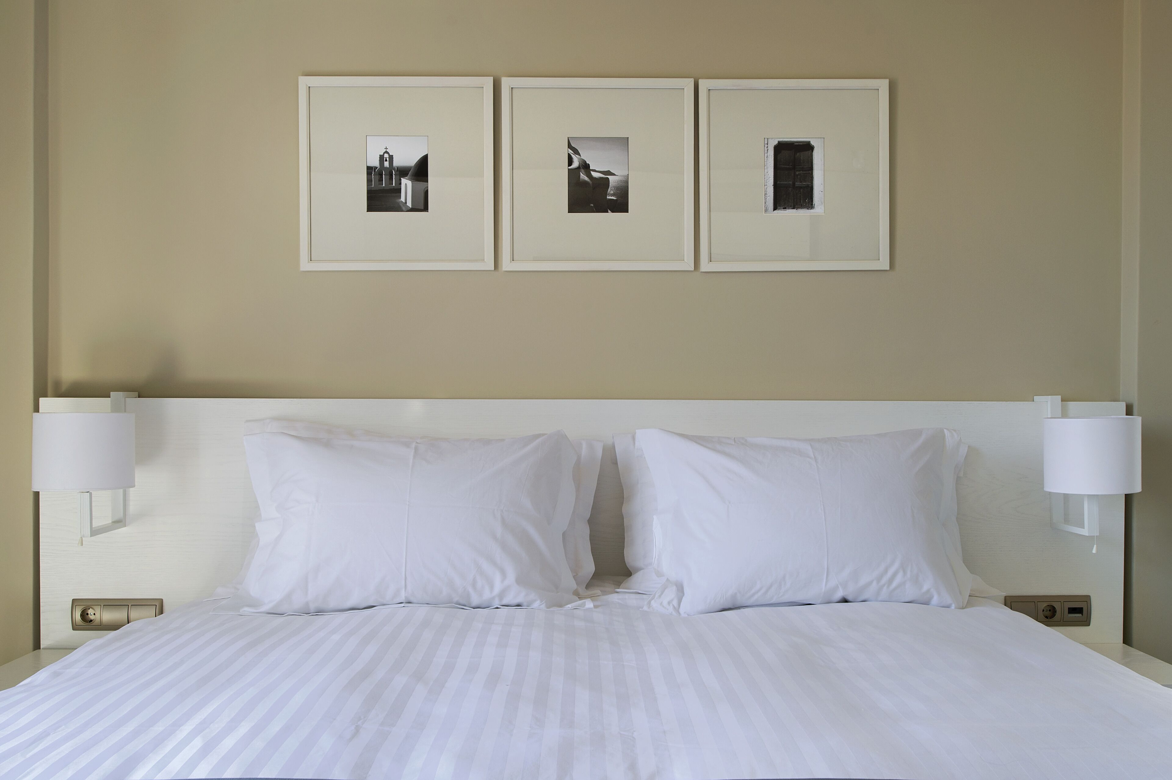 A hotel room with a large bed, two white pillows, a headboard, and three framed pictures on the wall.