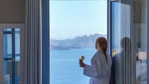 Una persona con bata blanca de pie junto a un amplio ventanal con vista al agua y montañas.