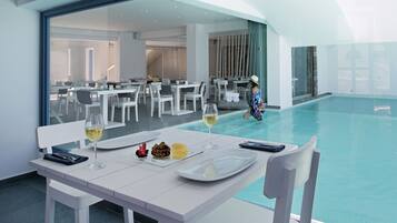 A dining area with white tables and chairs, a pool, and a person in a hat walking by.