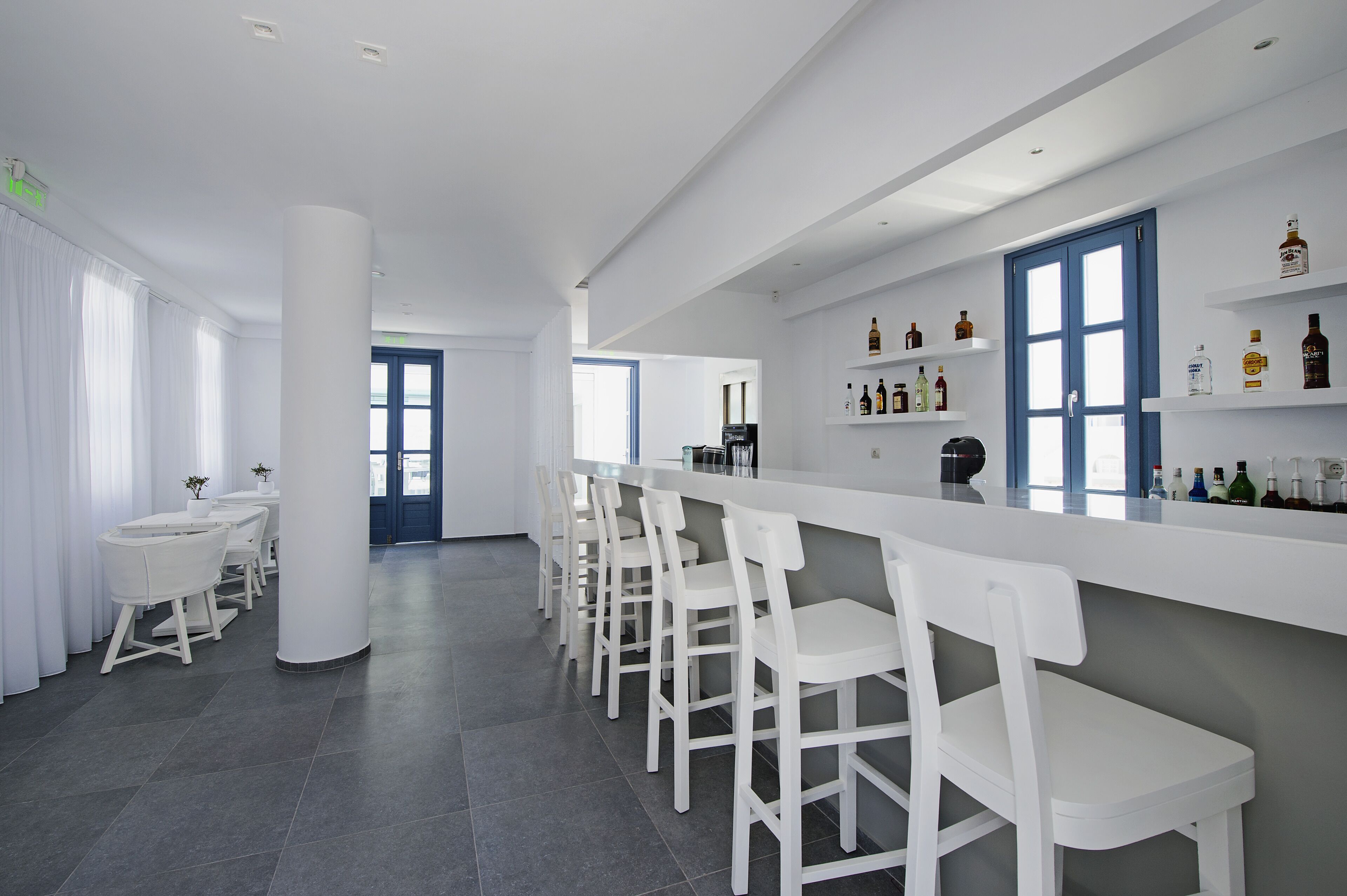 A modern bar area with white bar stools, a long counter, and shelves with bottles.