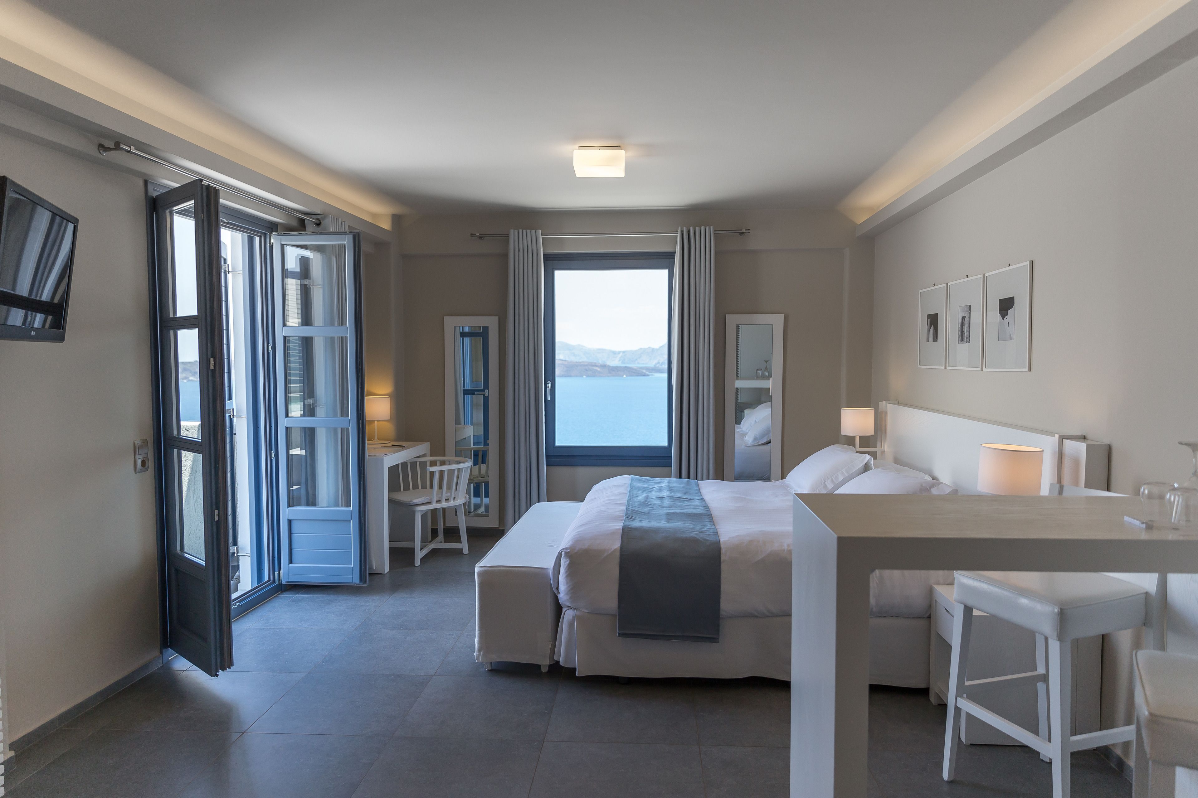 A modern hotel room with a large bed, a desk, and a view of the sea.