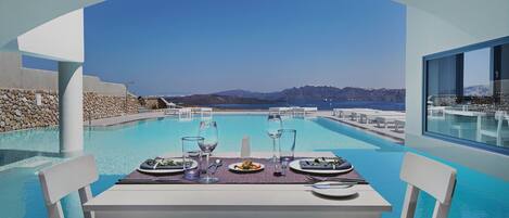 A dining table with chairs and a view of a pool and mountains.