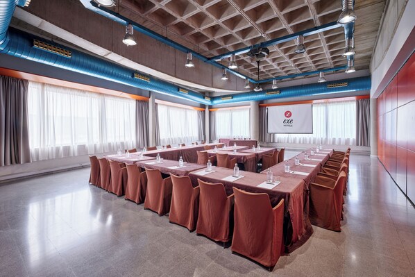 A conference room with long tables and chairs, large windows, and a visible logo on the wall.