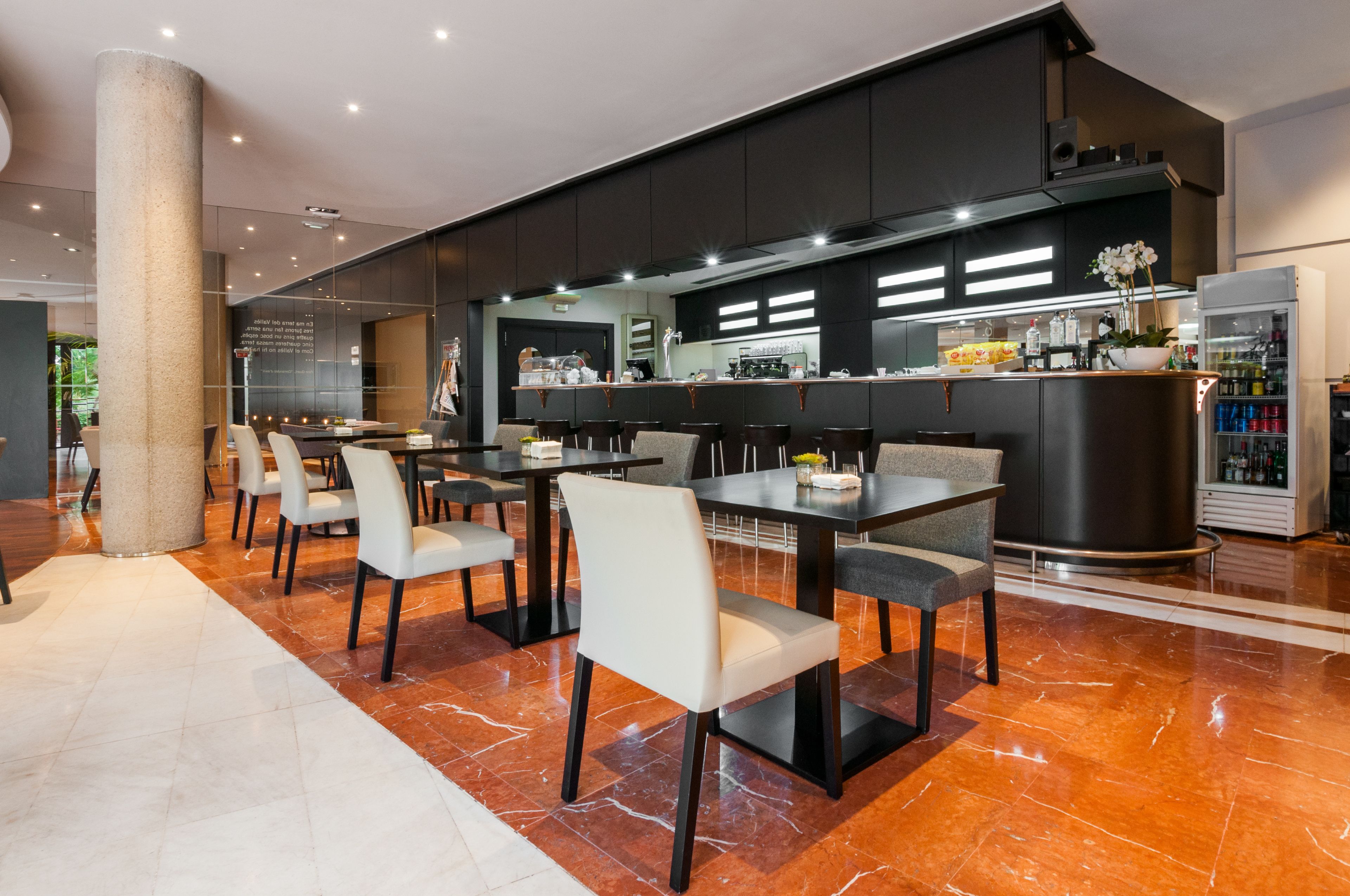 A modern restaurant with marble flooring, black and white chairs, and a central bar area.