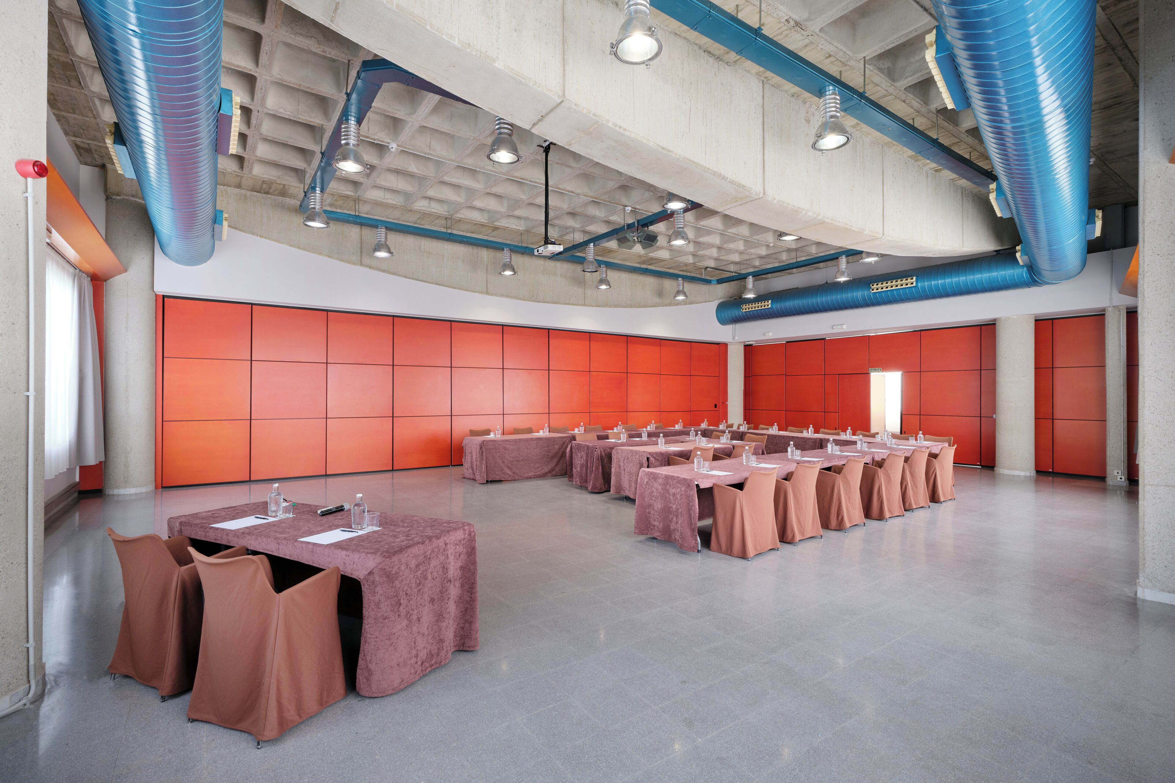 A spacious conference room with multiple tables and chairs, high ceilings with exposed ductwork, and a modern industrial design.