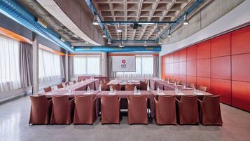 Un salón de conferencias con una larga mesa, múltiples sillas y una pared roja decorativa.
