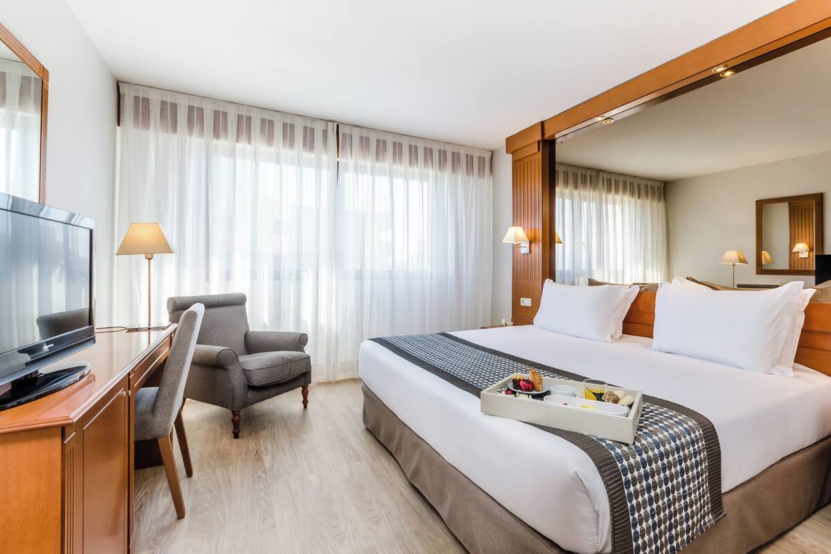 Une chambre d’hôtel avec un grand lit, un bureau avec une télévision, une chaise et un plateau contenant des articles pour le petit-déjeuner.