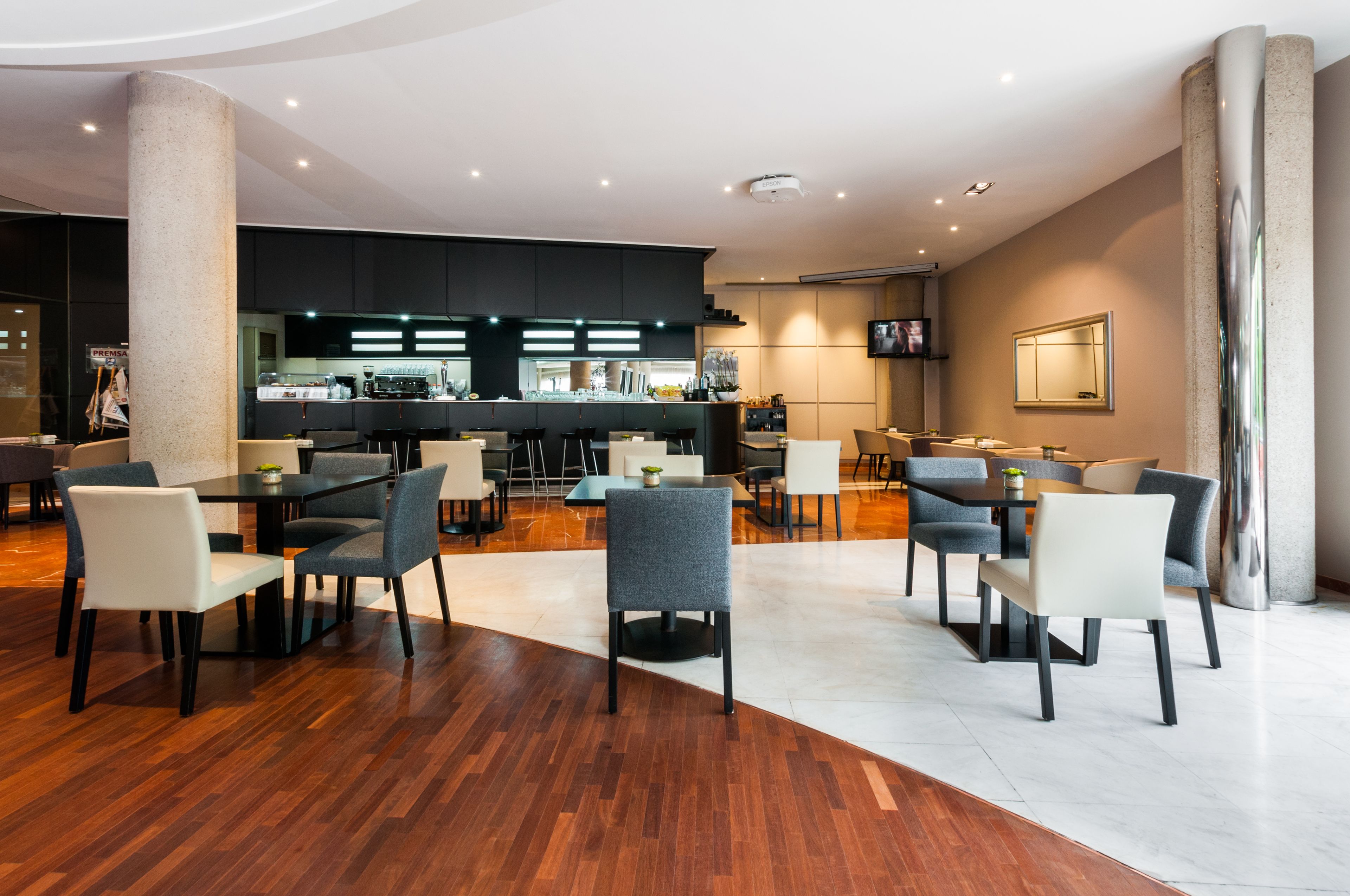 Um saguão de hotel moderno com área de bar, espaços para sentar e um pilar grande.