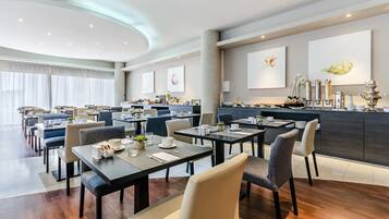 Un restaurante moderno con varias mesas y sillas, una zona de cocina y obras de arte en las paredes.