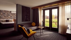 Una habitación de hotel moderna con sofá, un sillón amarillo, una mesita redonda y un ventanal con cortinas.