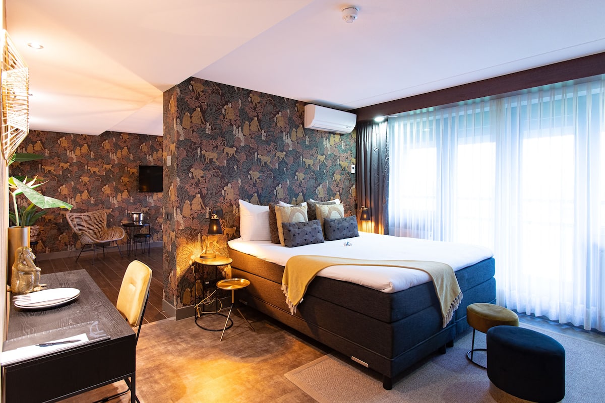 A modern hotel room with a large bed, a desk with a chair, a small table, and a sofa.
