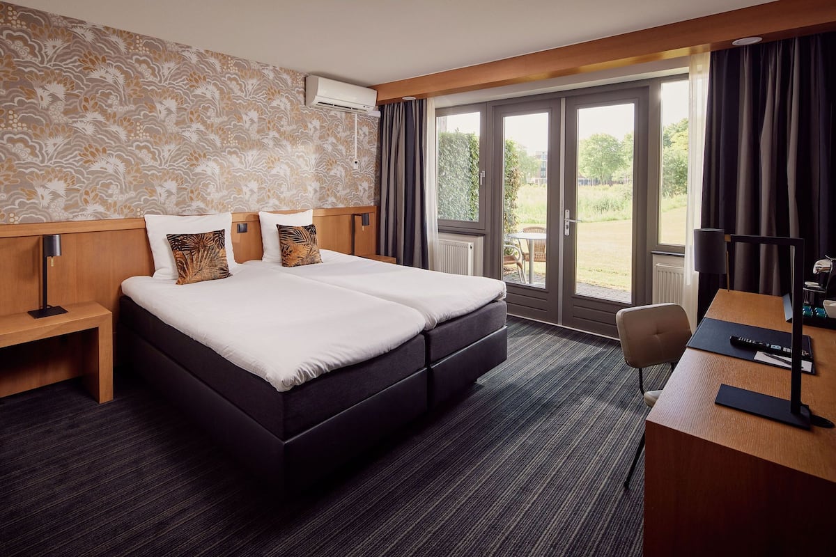 A hotel room with a large bed, a desk, and a view of the outdoors.