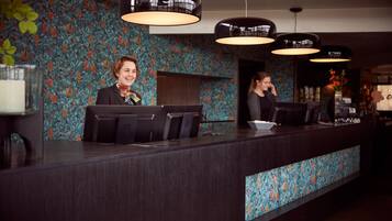 A reception desk with two staff members, a patterned wall, and pendant lighting.