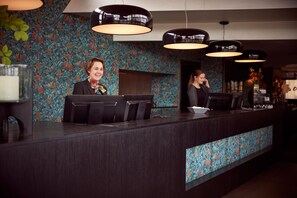 Una recepción con dos empleados, un papel tapiz decorativo e iluminación colgante.