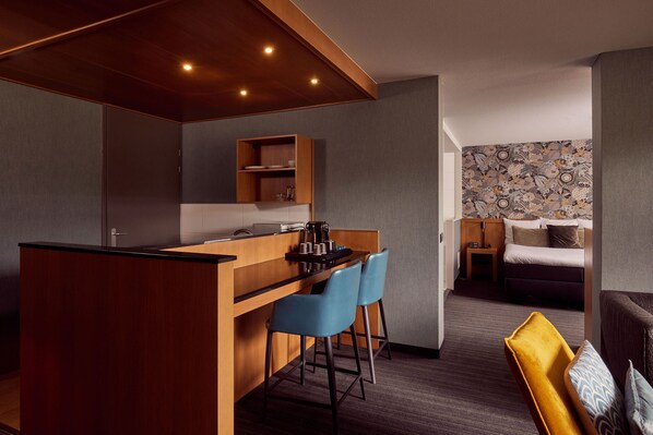 Habitación de hotel compacta con kitchenette, una cama, un escritorio pequeño y una zona de estar.