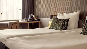 Een opgemaakt bed met gestreepte kussens, een bureau met een lamp en een wand met een geometrisch patroon.