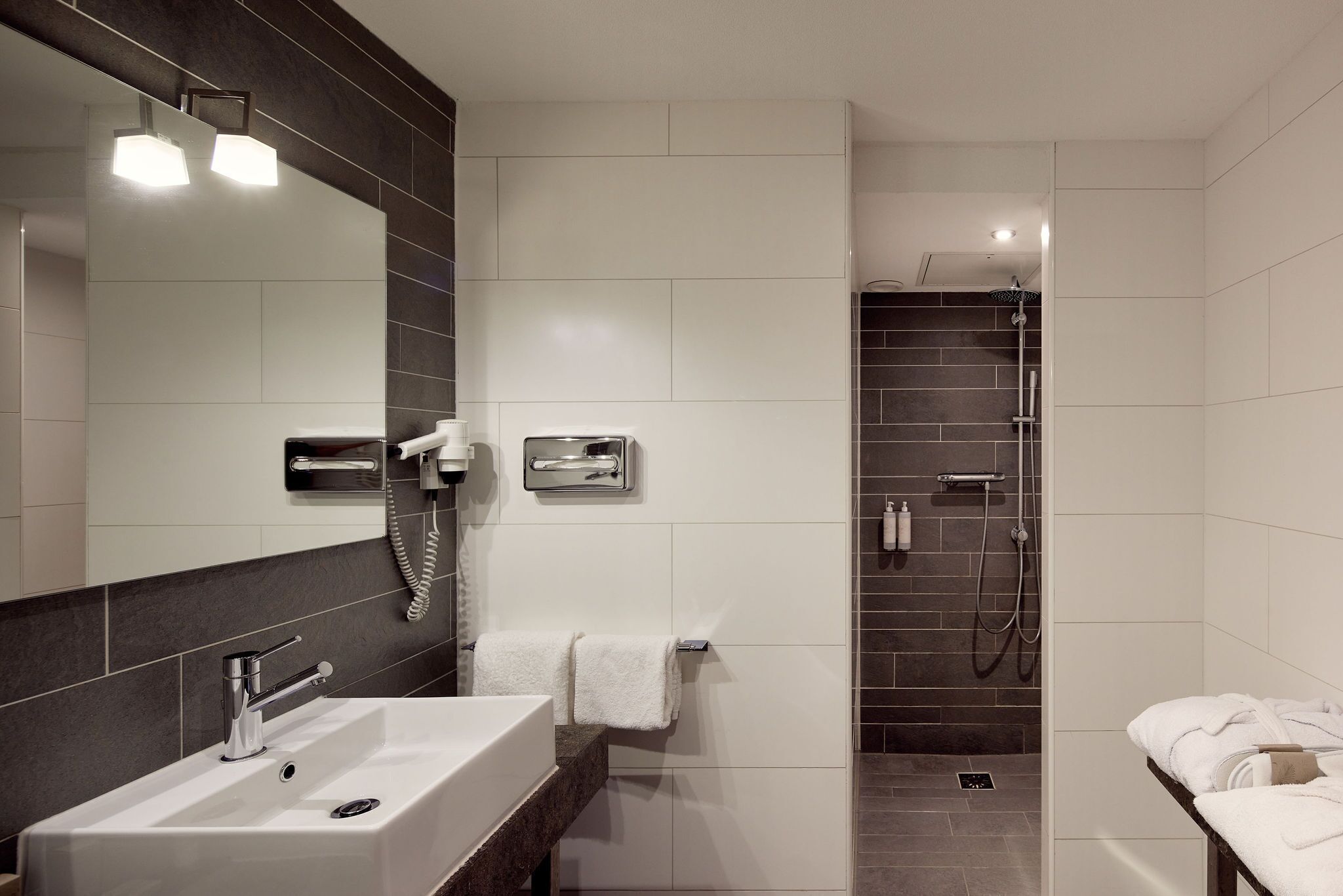 A modern bathroom with a large mirror, a sink, a shower area, and a towel rack.