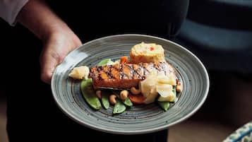 Una persona sosteniendo un plato con salmón a la parrilla, judías verdes, zanahorias y puré de patatas.
