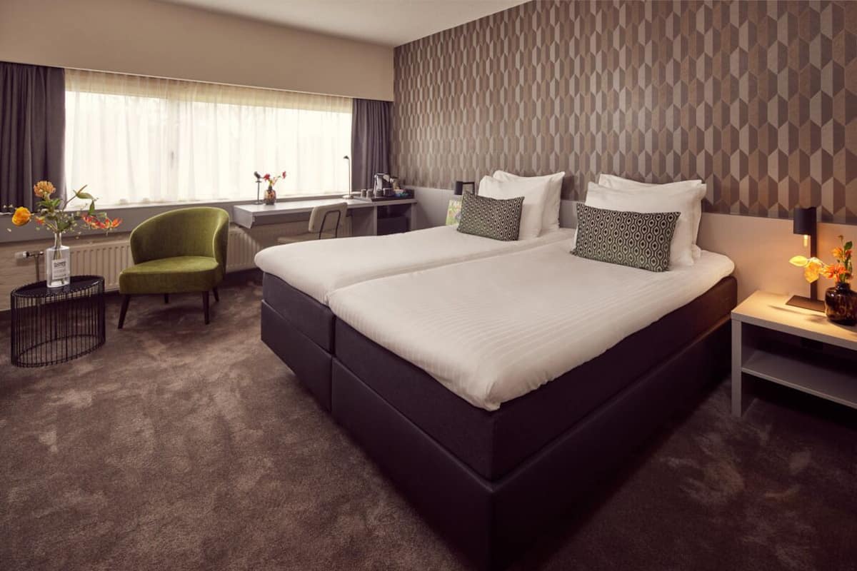 A hotel room with a large bed, a desk, a chair, and a view of the outdoors.