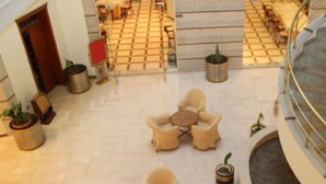 A hotel lobby with a tiled floor, seating areas with round tables and chairs, and potted plants. - Leonardo (Durres)
