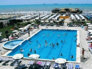 Uma grande piscina ao ar livre com várias pistas de natação, rodeada por espreguiçadeiras e guarda-sóis.