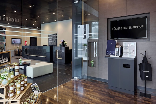 A modern hotel lobby with a reception desk, seating area, and a display of local products. - LEGERE HOTEL Tuttlingen (Tuttlingen)