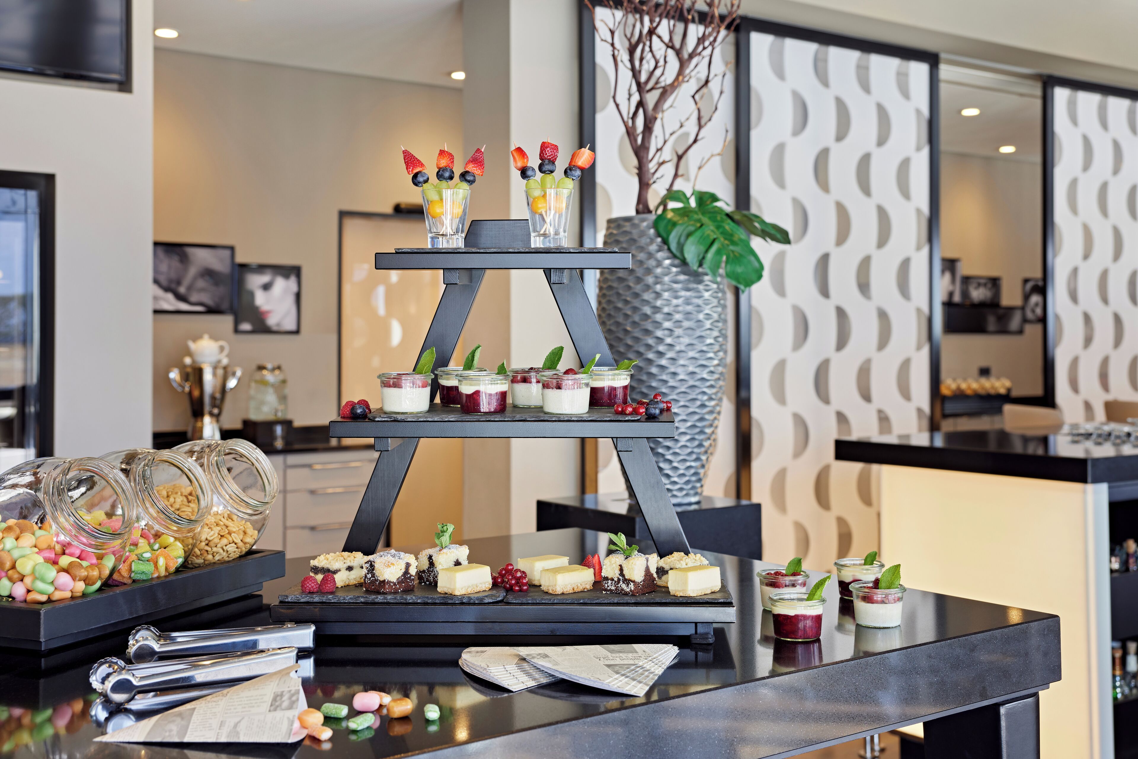A buffet table with various desserts and drinks, including jars of candies and small cups with fruit garnishes.