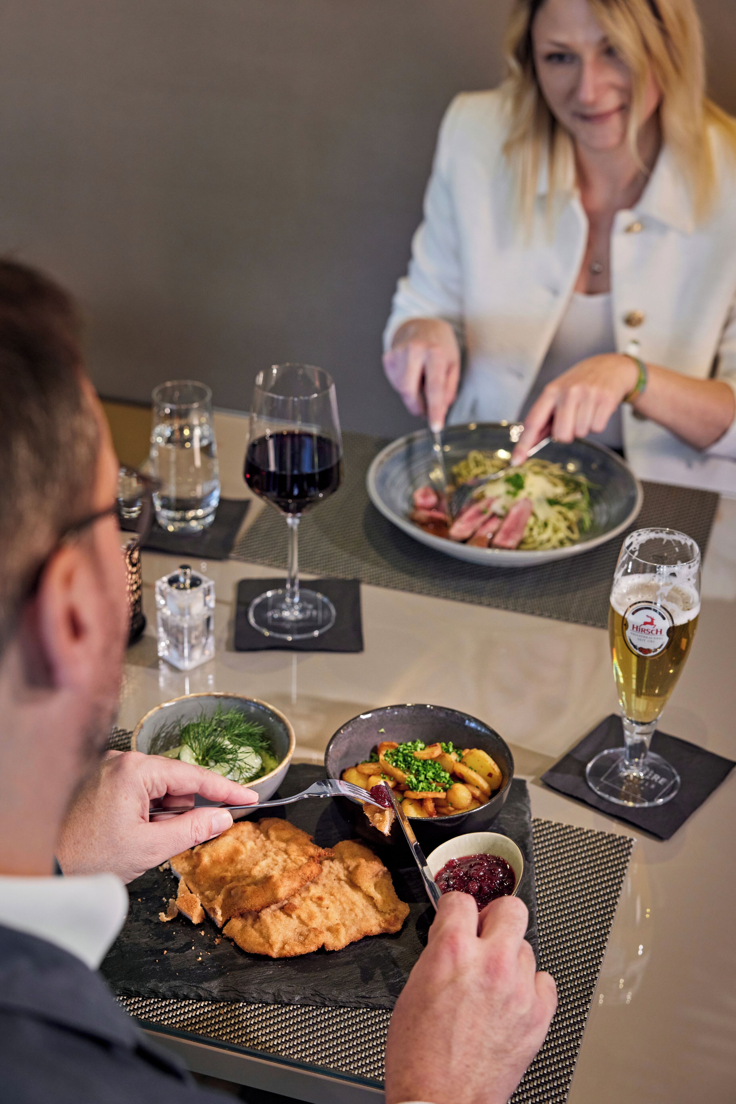 Una mesa de comedor con platos de comida, copas de vino y una jarra de cerveza.