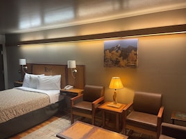Una habitación de hotel con una cama, dos mesitas de noche con lámparas, una mesita auxiliar de madera y un sofá de cuero marrón.