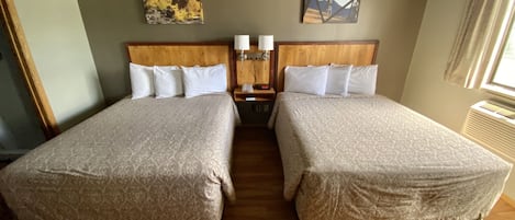 Ein Hotelzimmer mit zwei Betten, Holzboden, einem Nachttisch mit Lampe und zwei an der Wand hängenden Bildern.