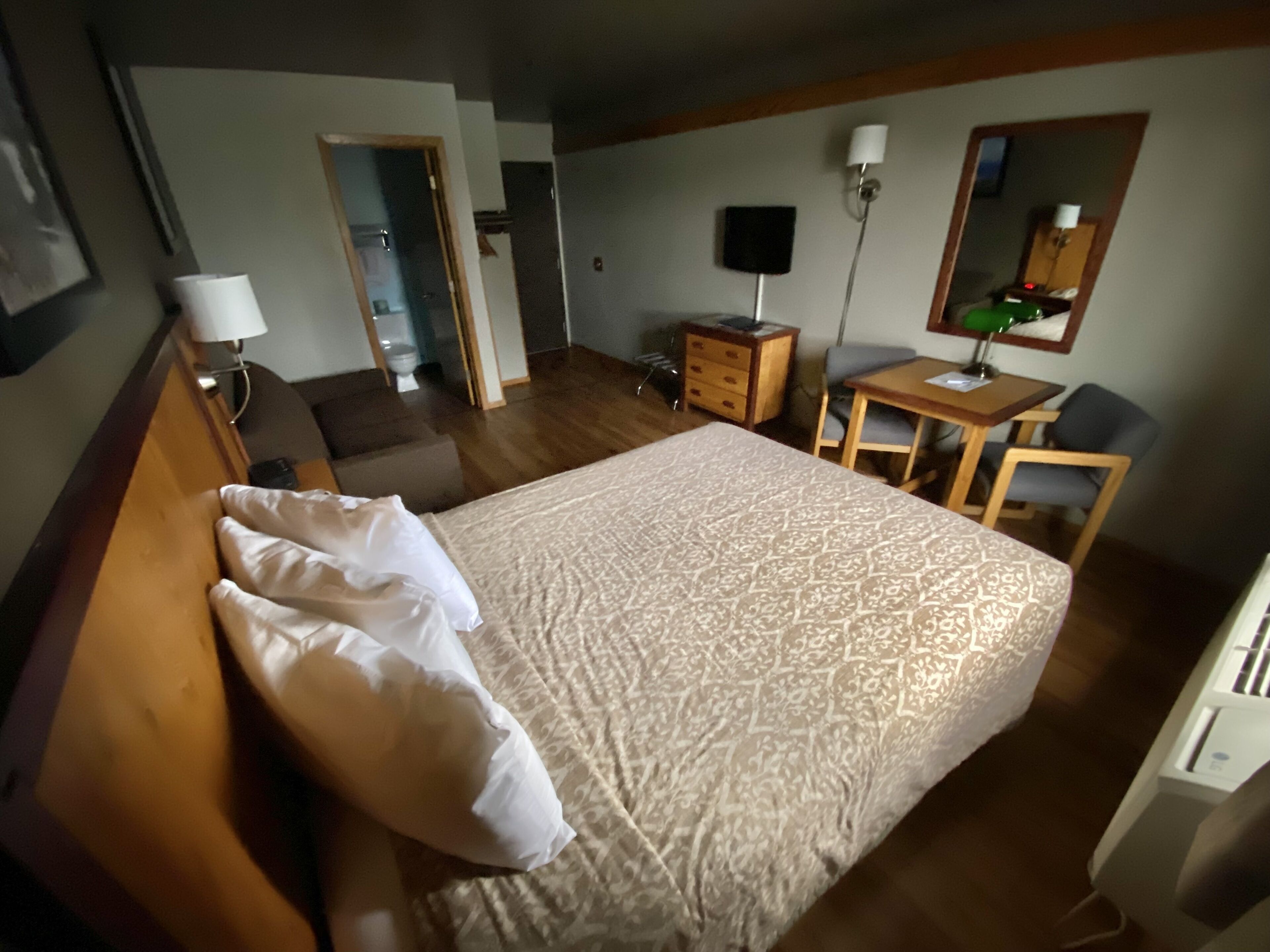 A hotel room with a large bed, a desk, a chair, a dresser, and a mirror.