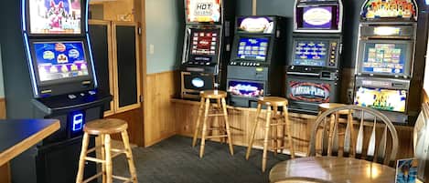 A bar area with slot machines, wooden stools, and a table.