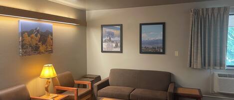 A cozy living room with a sofa, two armchairs, a coffee table, and a lamp. There are three framed pictures on the wall.