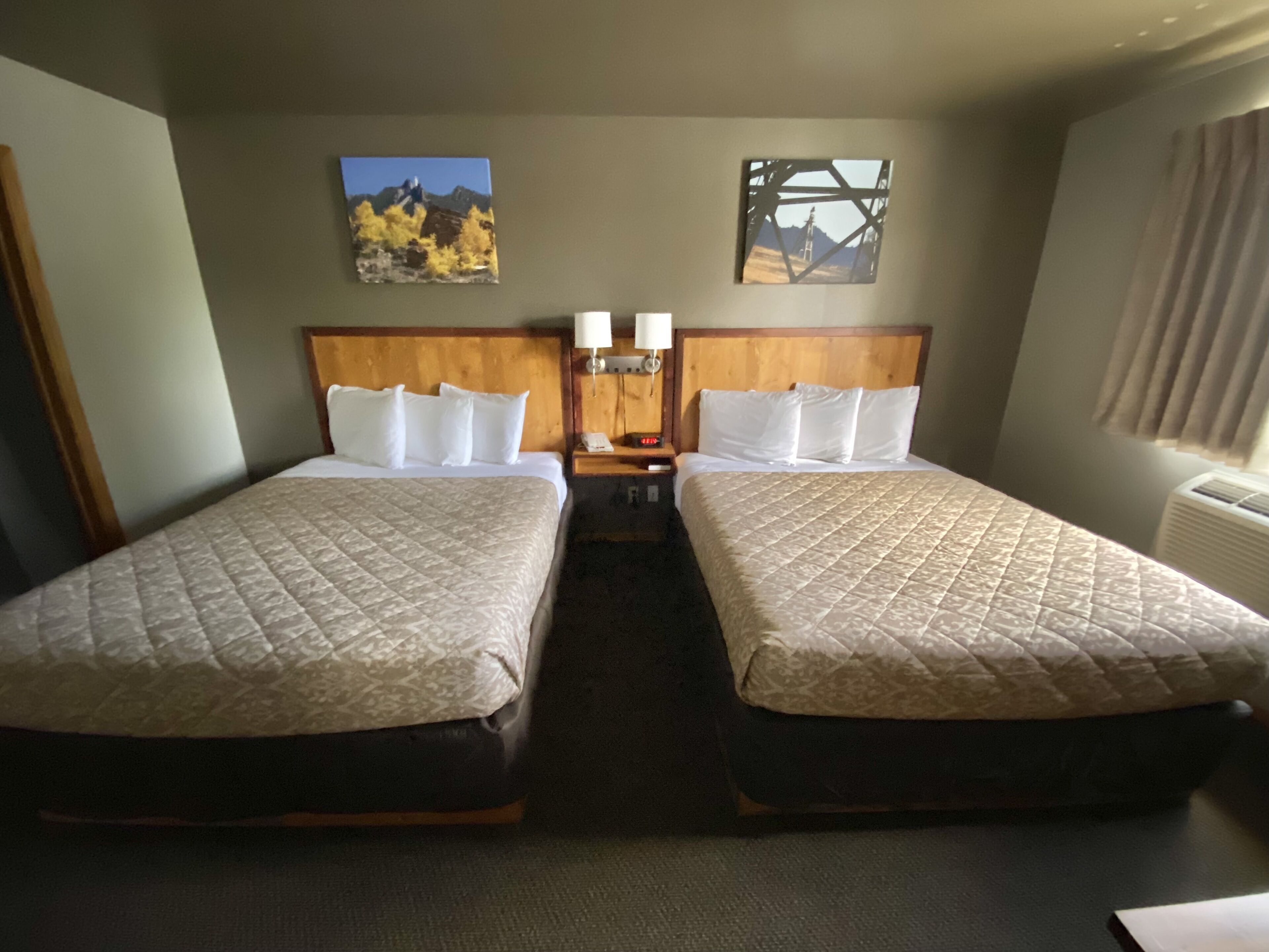 Ein Hotelzimmer mit zwei Betten, einem Holzkopfteil, einem Nachttisch mit Lampe und zwei Bildern an den Wänden.