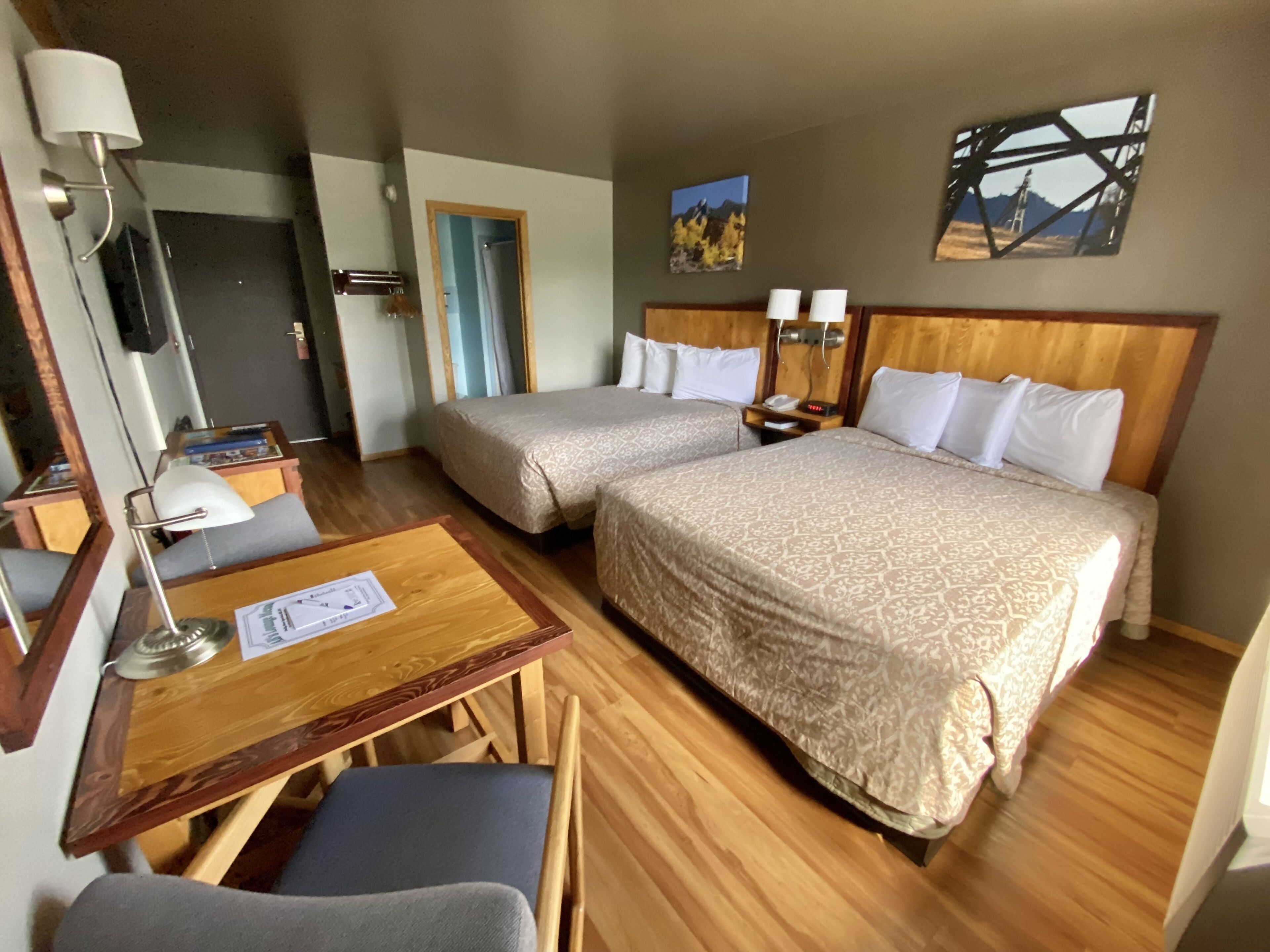 Une chambre d’hôtel avec deux lits, un bureau, une chaise, une lampe et un tableau au mur.