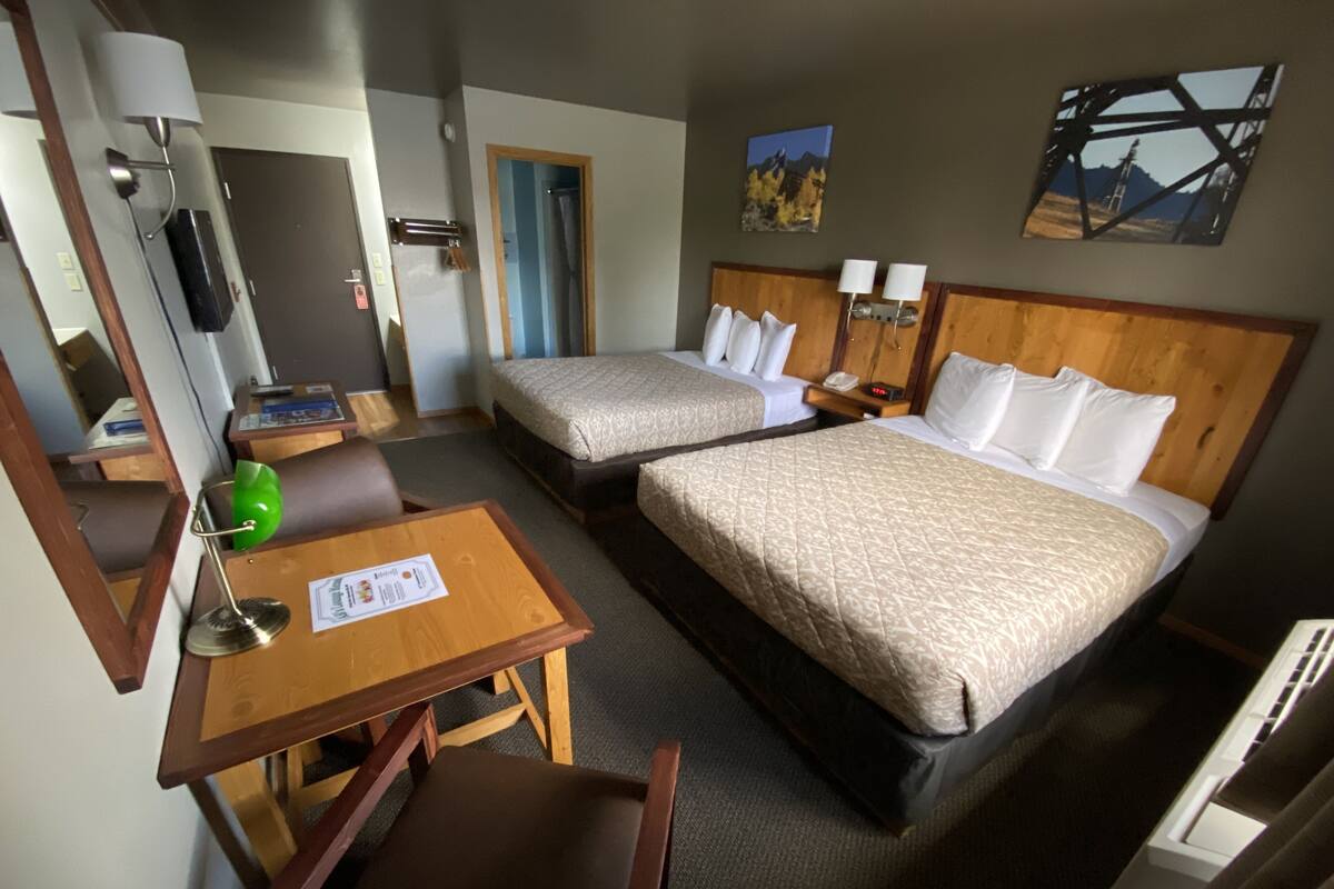 A hotel room with two beds, a desk, a chair, a lamp, a mirror, and a painting on the wall.