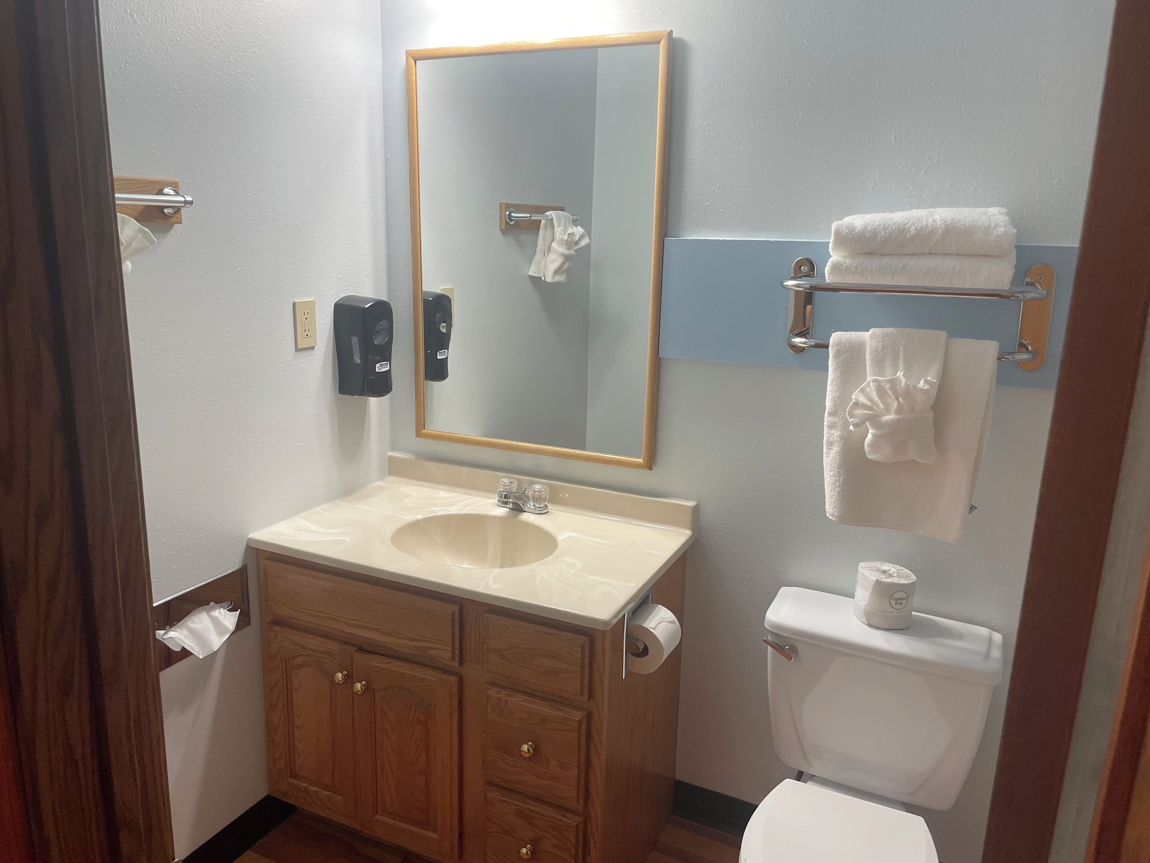 A bathroom with a sink, mirror, towel rack, toilet, and wooden cabinets.