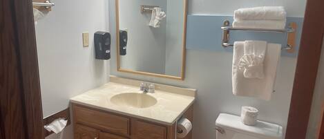A bathroom with a sink, mirror, towel rack, toilet, and wooden cabinets.