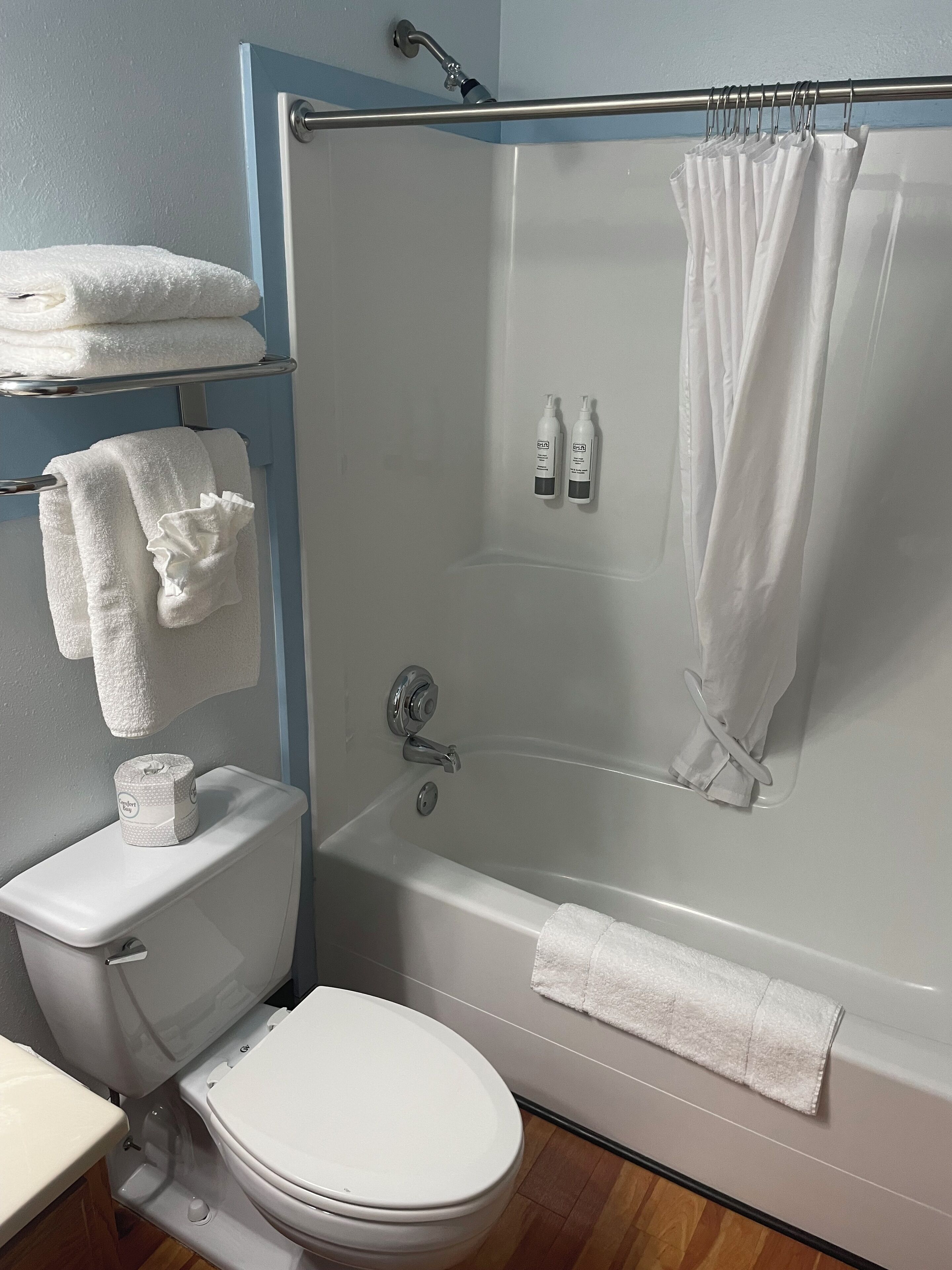 Um banheiro com vaso sanitário branco, banheira com cortina de chuveiro e duas garrafas de shampoo na parede.