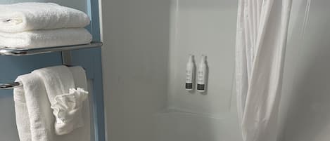 Un baño con un inodoro blanco, una bañera con cortina de ducha y dos botellas de champú en la pared.