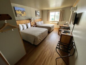 A hotel room with two beds, a desk, a chair, a TV, and a window with curtains.