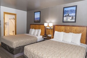 A hotel room with two beds, wooden headboards, a nightstand with a phone, and framed pictures on the wall.