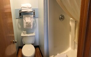 A bathroom with a toilet, a towel rack with folded towels, and a shower curtain.